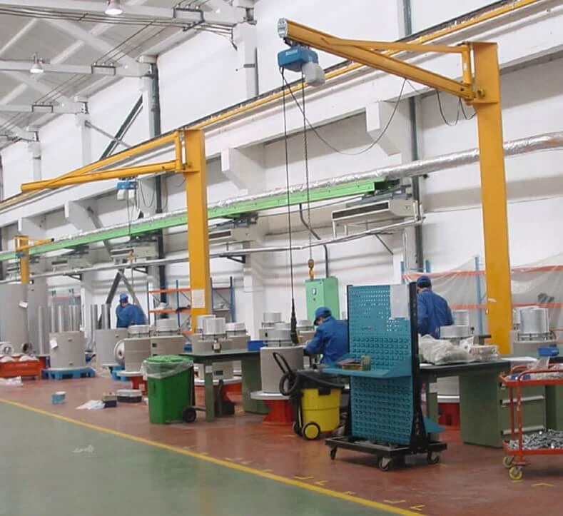 Machine shop bay served by yellow pillar jib cranes with operators at workstations